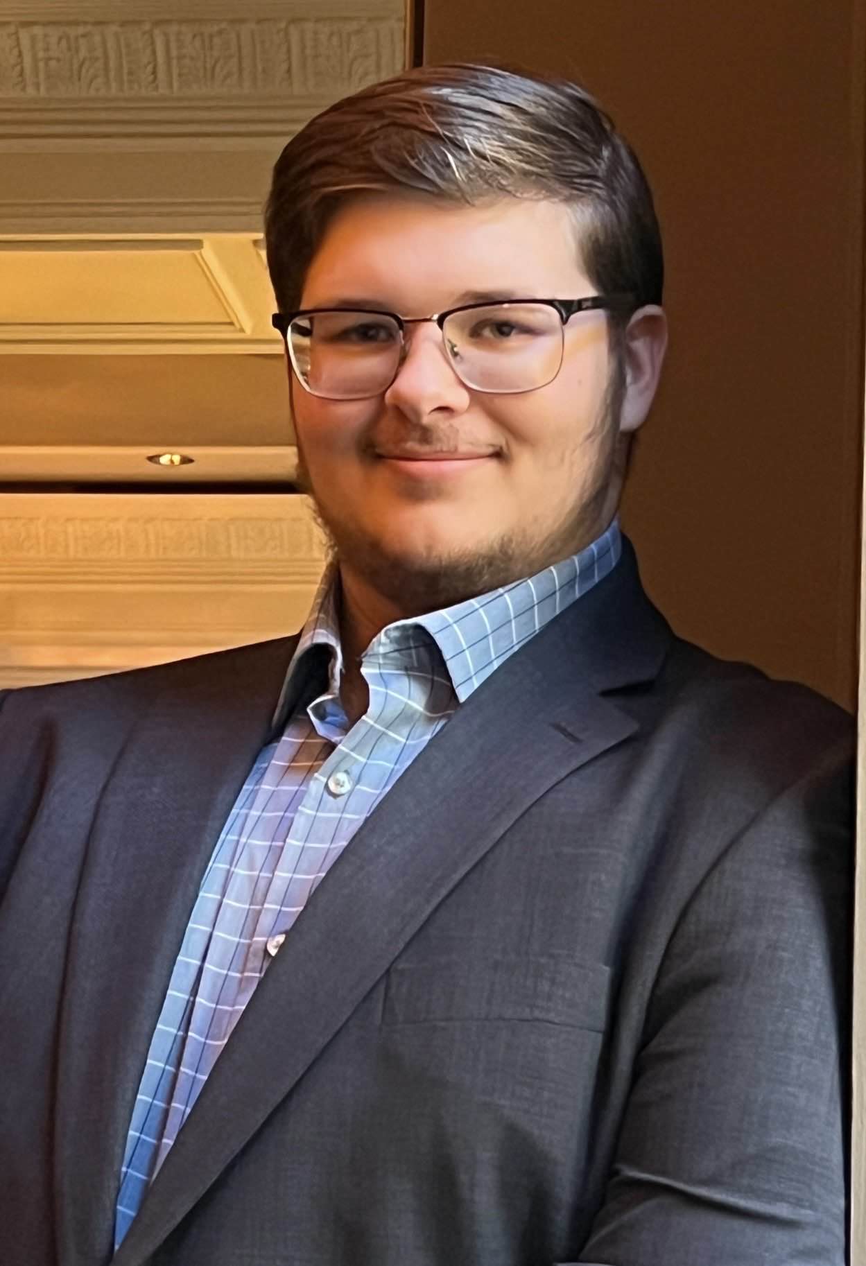 Portrait of Caden Trahan in a dark suit indoors.